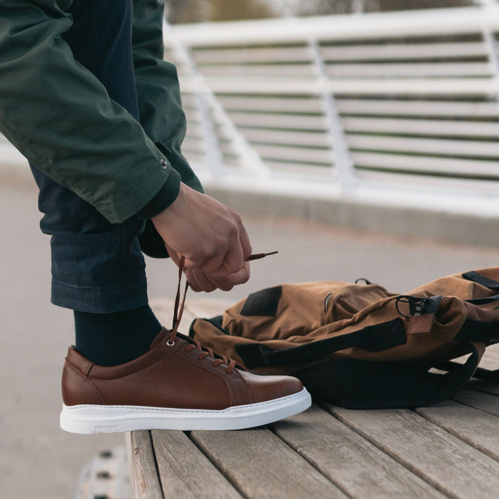 Person tying their men's brown sneakers.